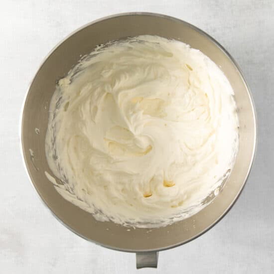 Whipped cream in a metal bowl on a white background.