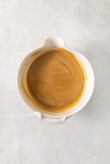 A bowl of caramel sauce on a white surface.