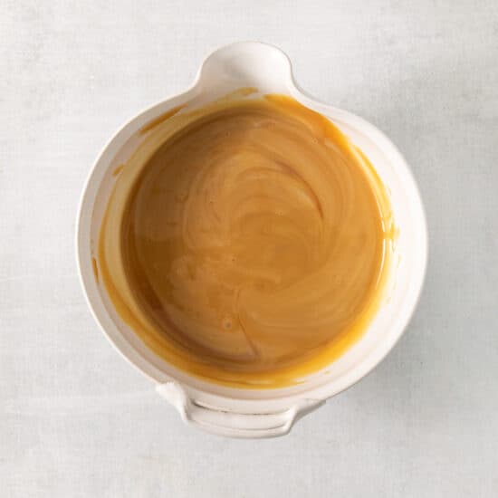 A bowl of caramel sauce on a white surface.