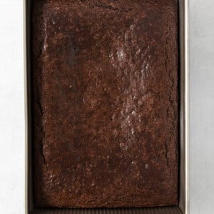 A brownie in a metal pan on a white surface.