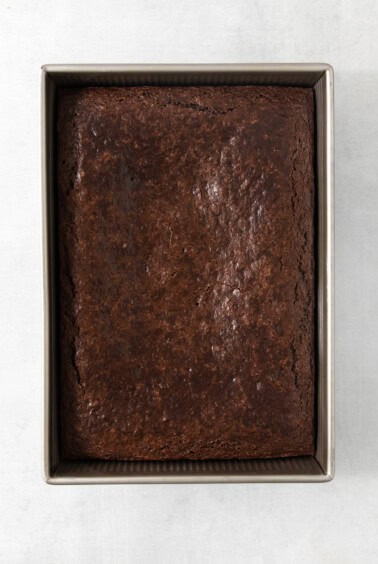 A brownie in a metal pan on a white surface.