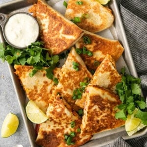 Quesadillas on a baking sheet with lime wedges.