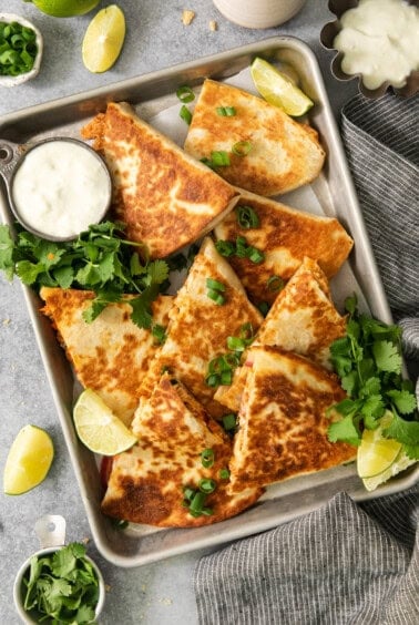 Quesadillas on a baking sheet with lime wedges.