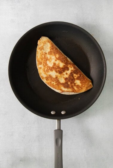 A quesadilla is being cooked in a frying pan.