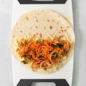 A taco on a cutting board with carrots and onions.