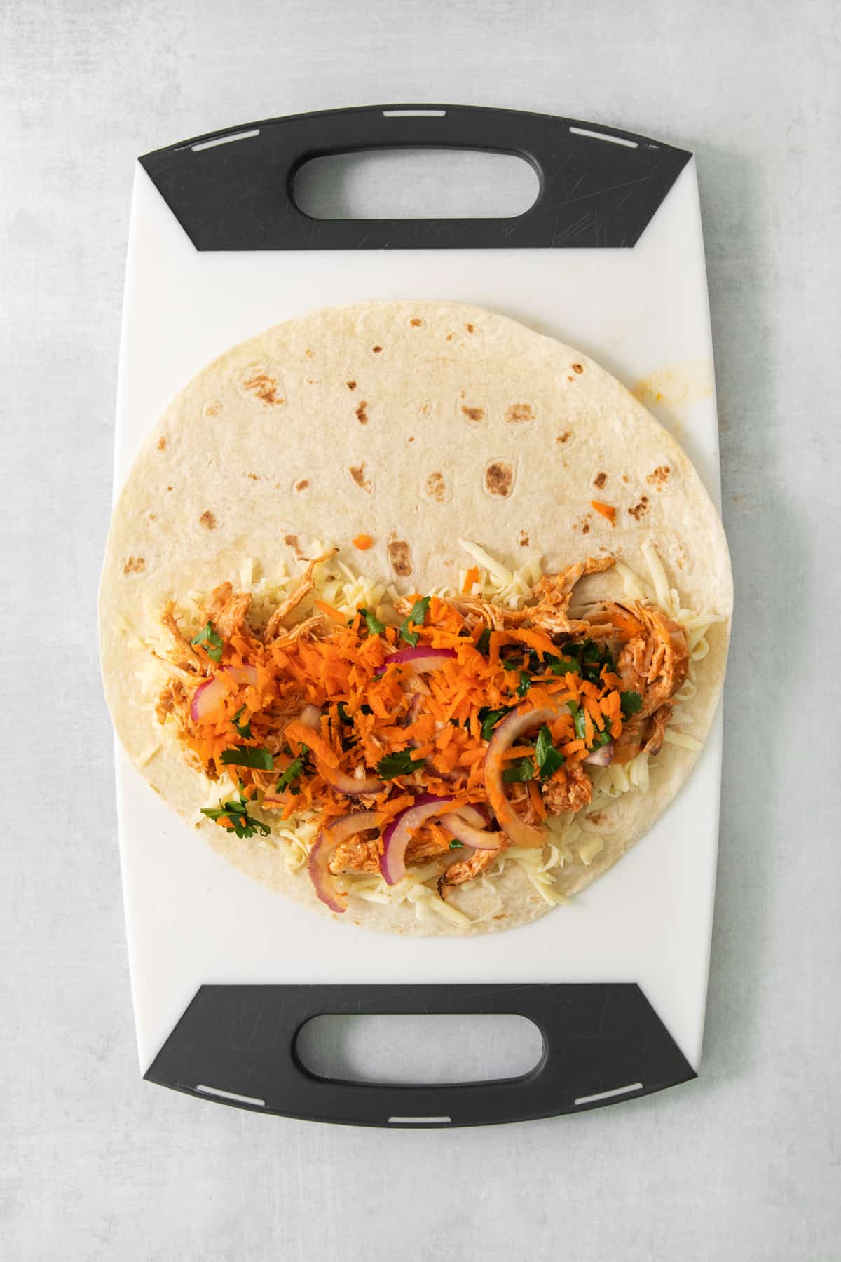 A taco on a cutting board with carrots and onions.