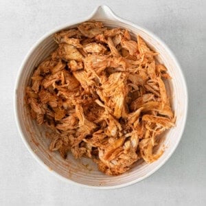 Shredded chicken in a white bowl on a grey background.