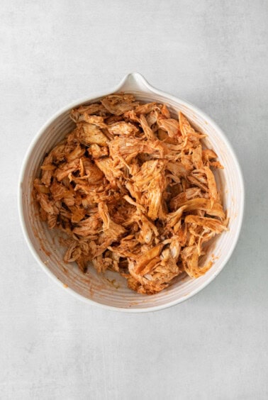 Shredded chicken in a white bowl on a grey background.