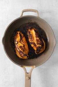 A frying pan with two chicken breasts in it.