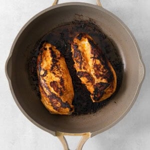 A frying pan with two chicken breasts in it.