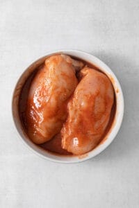 Two chicken breasts in a bowl on a white surface.