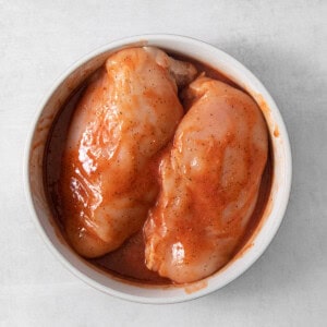 Two chicken breasts in a bowl on a white surface.