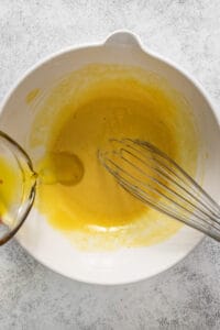 A white bowl with a whisk and yellow liquid.