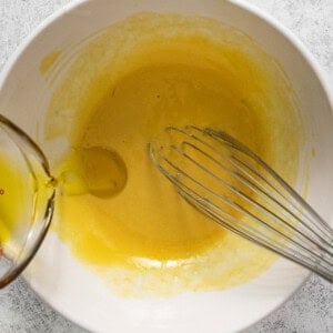 A white bowl with a whisk and yellow liquid.