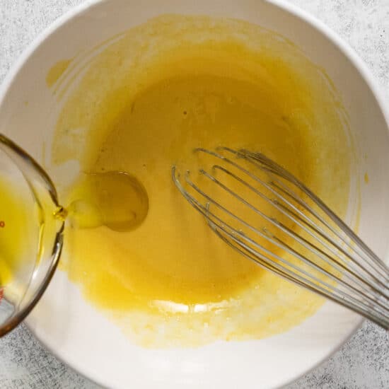 A white bowl with a whisk and yellow liquid.