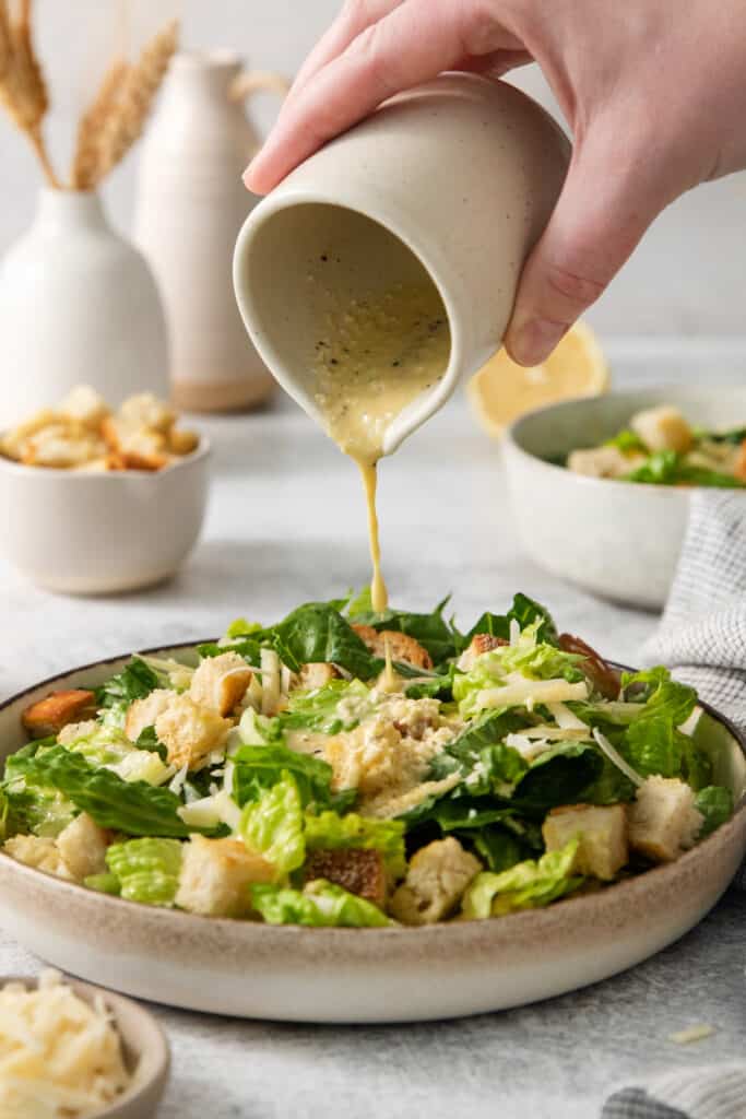 A person pouring a dressing on a salad.