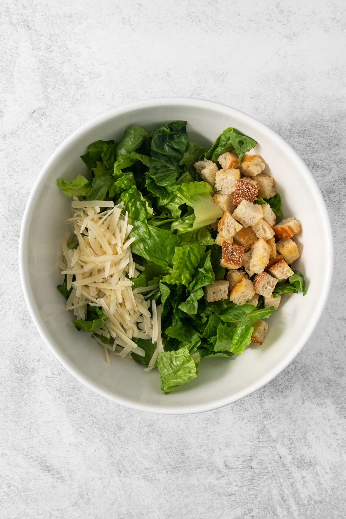 Caesar salad with croutons and croutons in a white bowl.