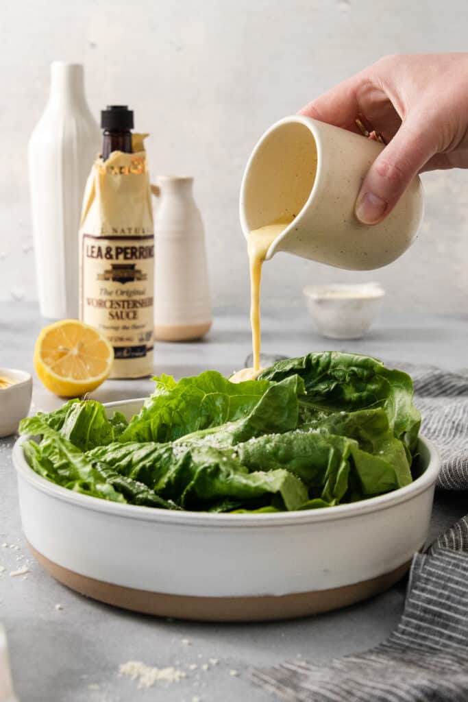 A person pouring a dressing on a salad.