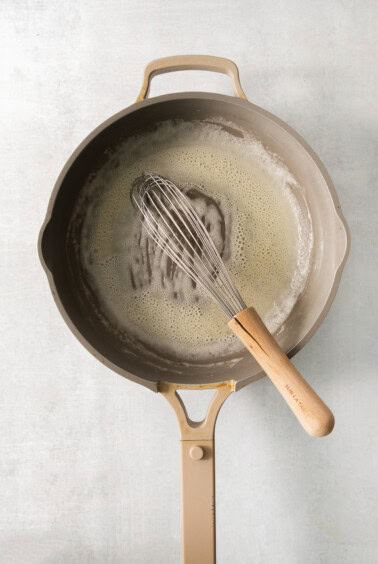 A frying pan with a whisk in it.