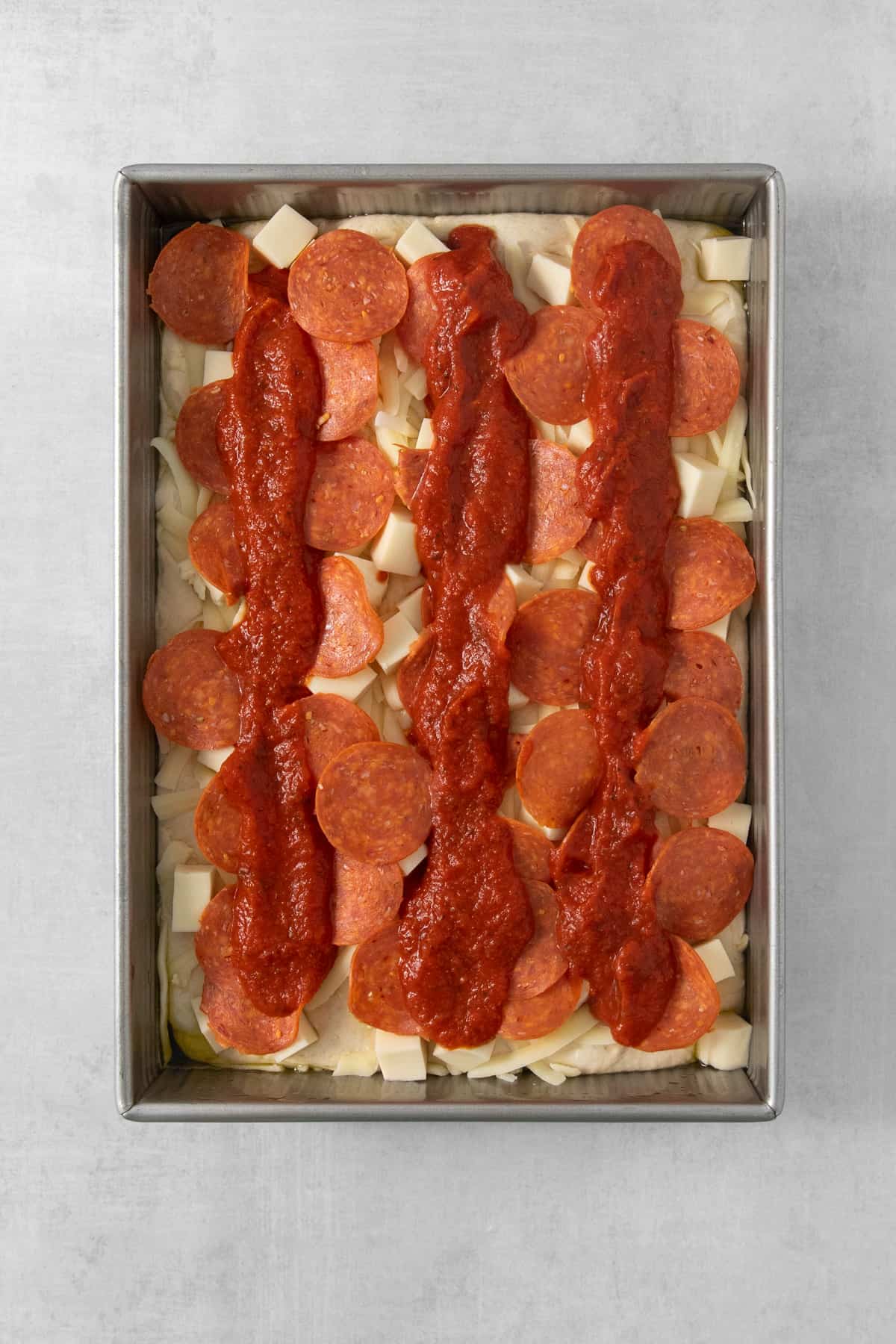 A pizza with pepperoni and sauce in a metal pan.