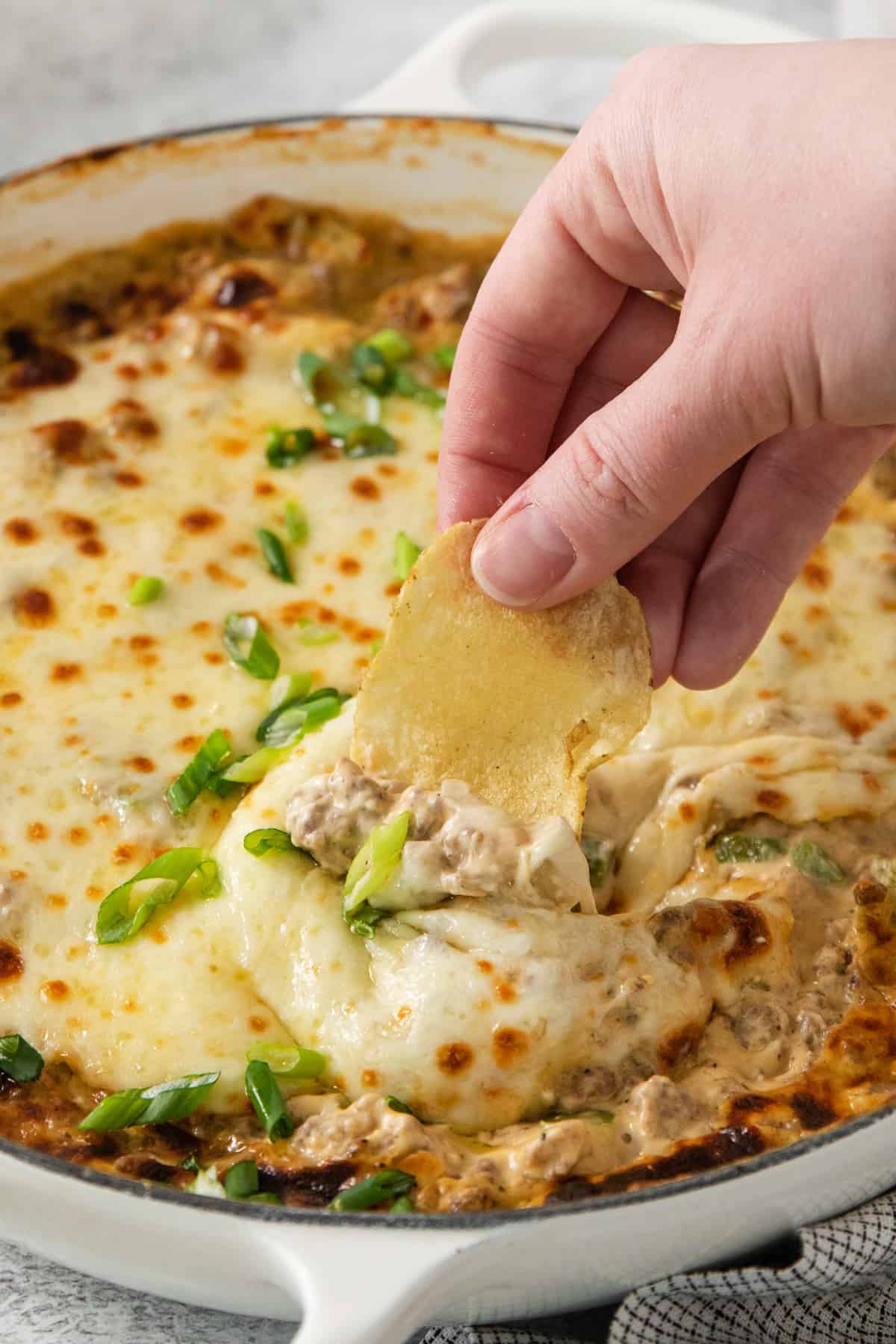 A person dipping a chip into a dish of chicken dip.