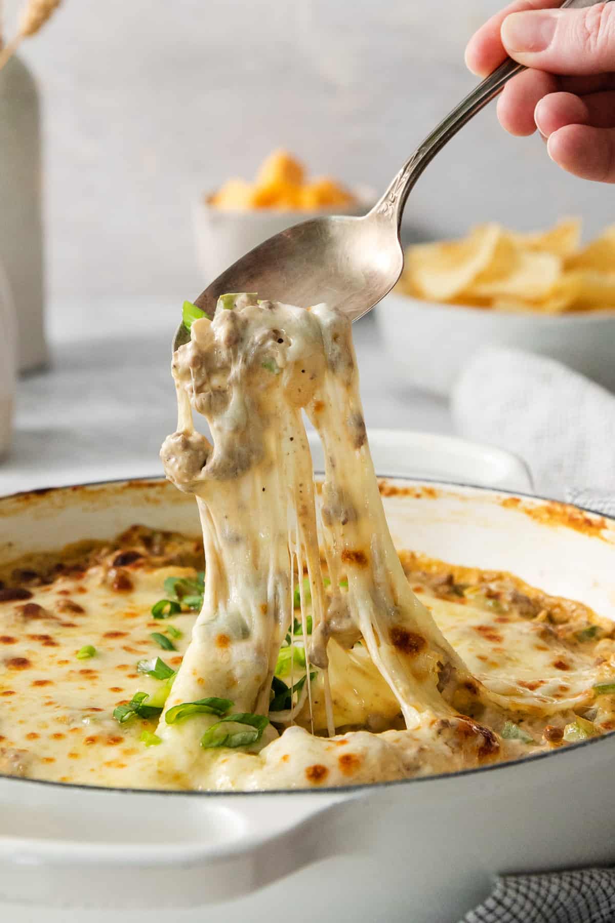 A person dipping a spoon into a dish of cheese dip.