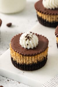 Close-up of an espresso cheesecake cup with Oreo crust, chocolate ganache, and whipped cream on a marble board.