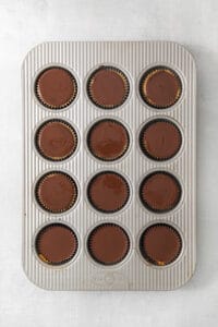 Overhead view of twelve espresso cheesecake cups topped with chocolate ganache in a muffin tin.