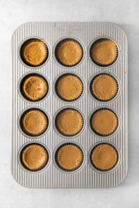 Twelve espresso cheesecake cups filled with coffee cheesecake batter in a muffin tin.