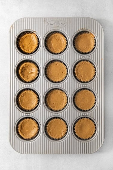 Twelve espresso cheesecake cups filled with coffee cheesecake batter in a muffin tin.