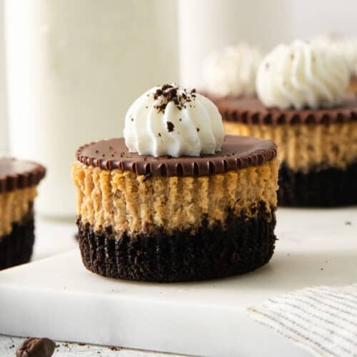 Espresso cheesecake cups with Oreo cookie crust, chocolate ganache, and whipped cream on a marble serving board.