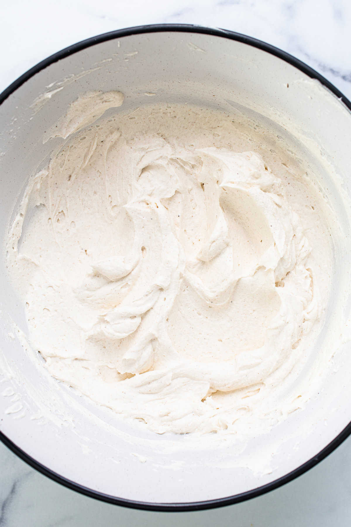 Whipped cream in a bowl on a marble countertop.