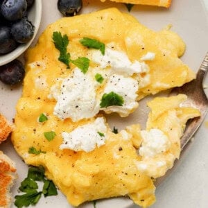 A plate of goat cheese scrambled eggs with blueberries and sour cream.