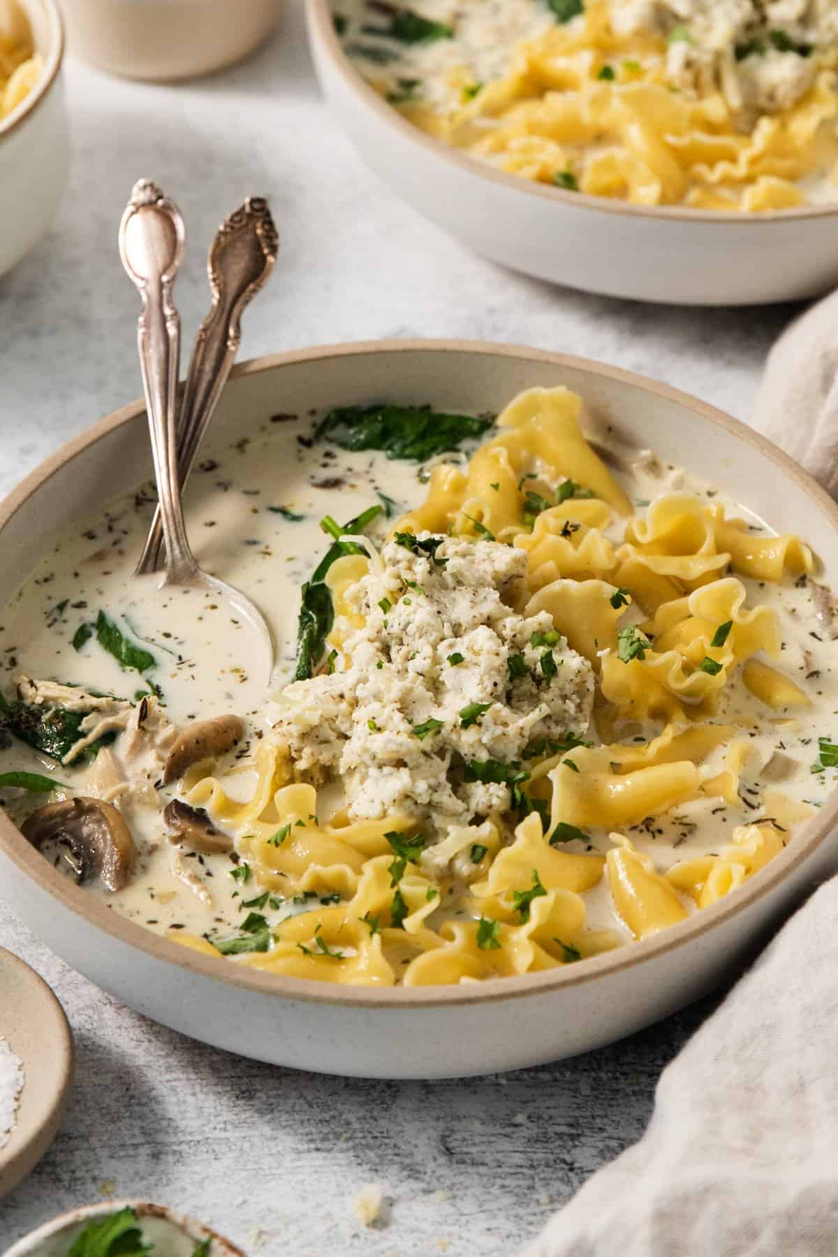 Two bowls of soup with noodles and spinach.