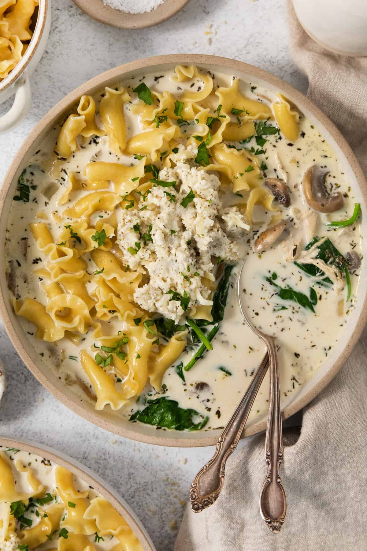 A bowl of pasta soup with spinach and mushrooms.