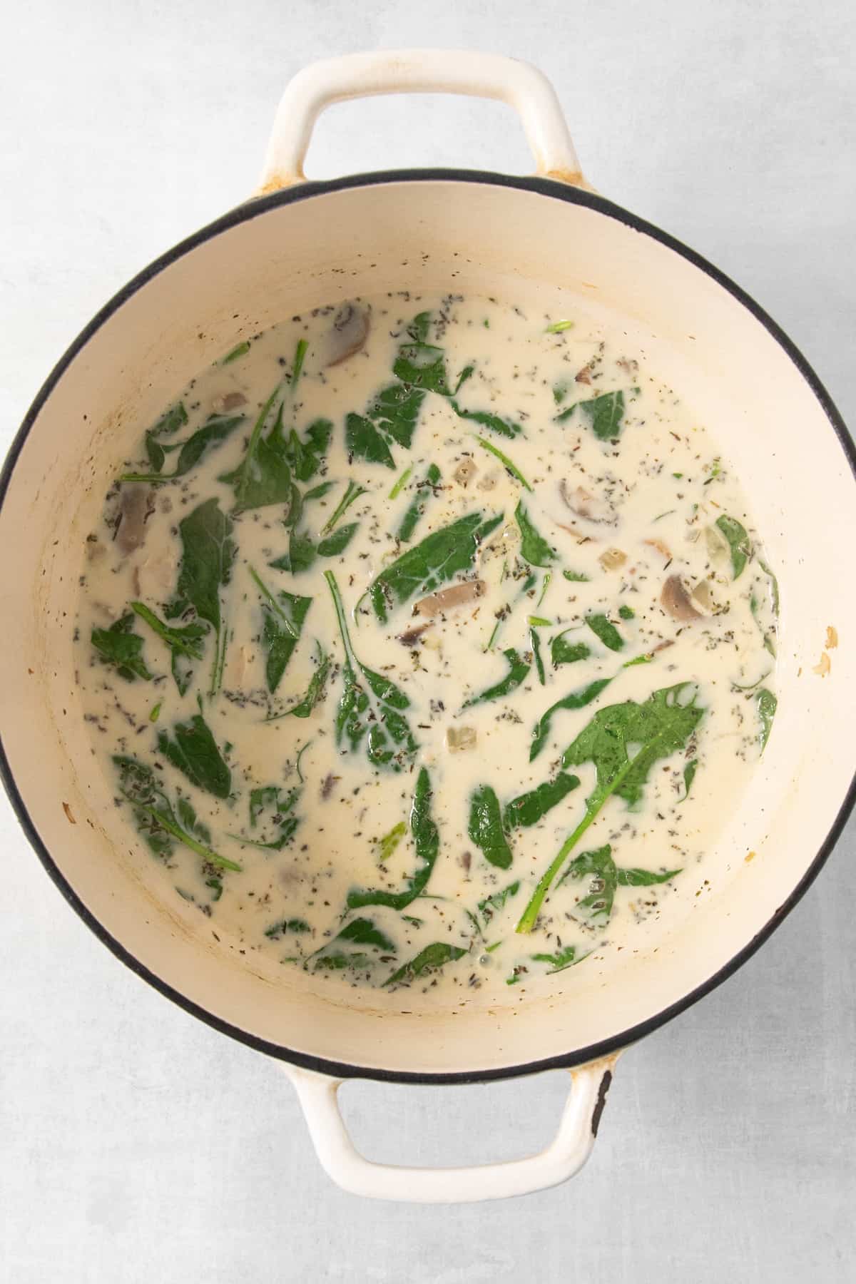 A pot of soup with spinach and mushrooms.