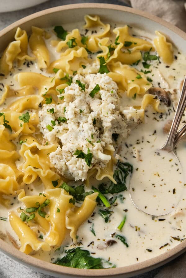 A bowl of pasta soup with spinach and cheese.