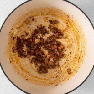 Sautéed diced ingredients with remnants in a white enameled dutch oven.