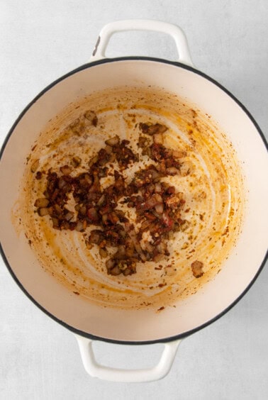 Sautéed diced ingredients with remnants in a white enameled dutch oven.