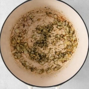 Sautéed diced onions and herbs in a white enameled cast iron pot.