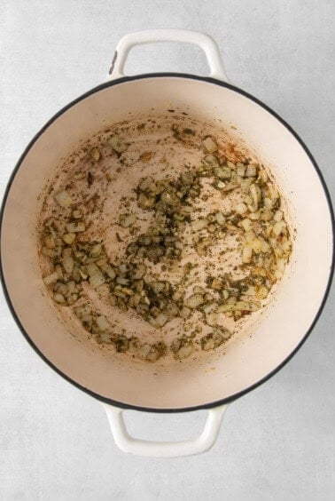 Sautéed diced onions and herbs in a white enameled cast iron pot.