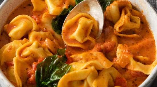 A bowl of tortellini in tomato cream sauce with spinach, served with a spoon.