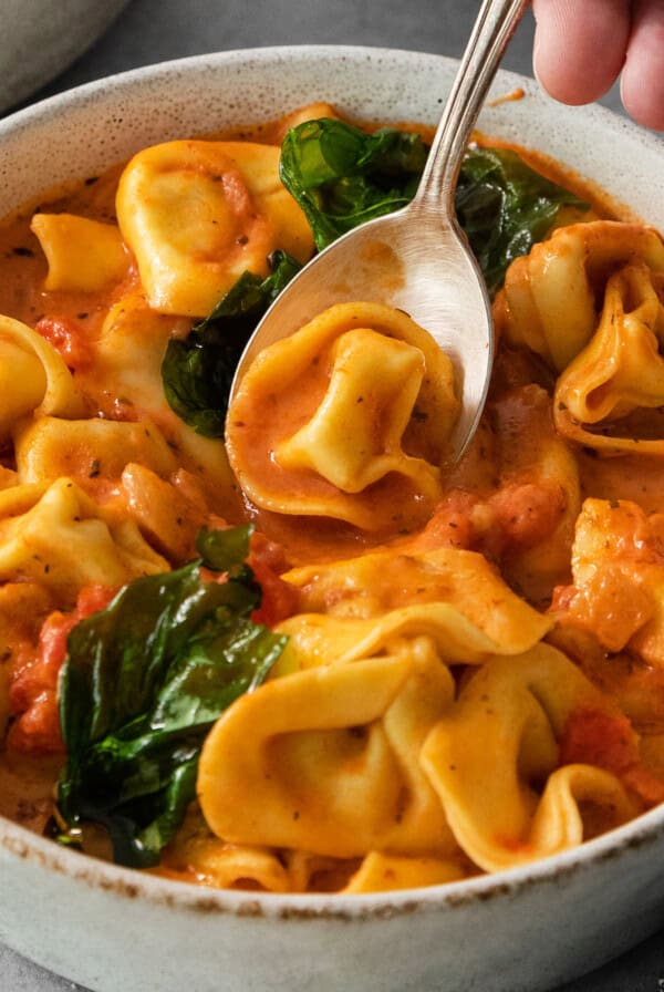 A bowl of tortellini in tomato cream sauce with spinach, served with a spoon.