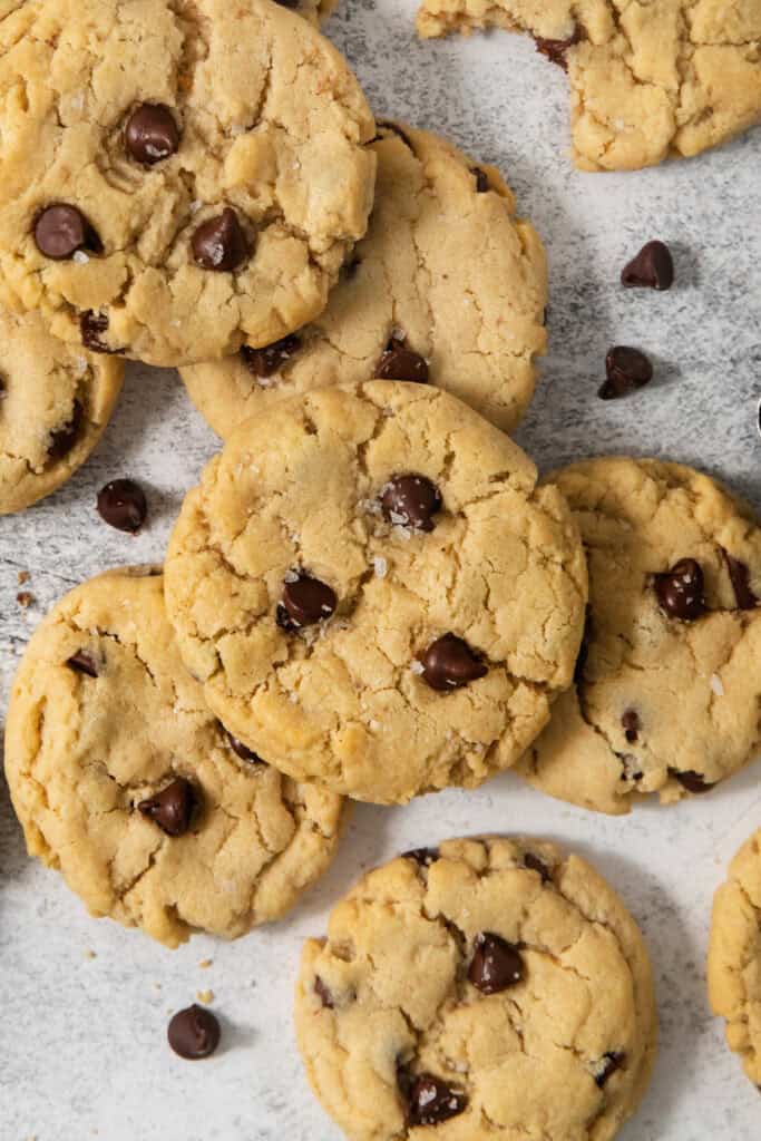 A close-up of several egg-free chocolate chip cookies scattered on a white surface, with some chocolate chips strewn around them.