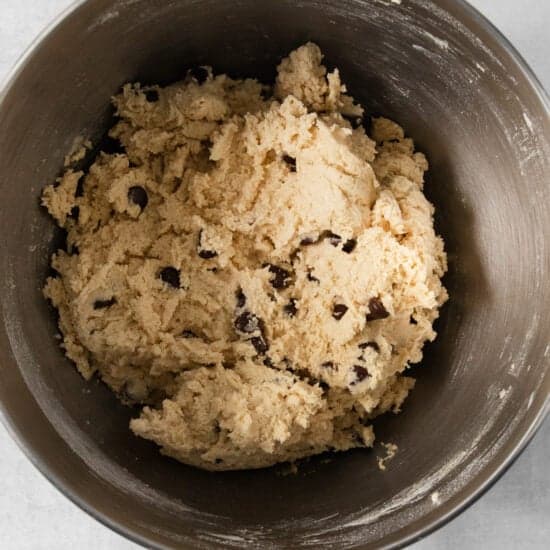 A bowl of egg-free chocolate chip cookie dough sits invitingly on a light-colored surface.