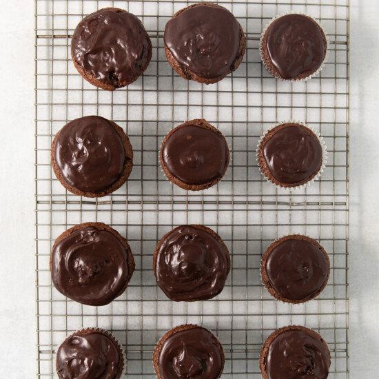 A cooling rack holds 15 chocolate-frosted cupcakes arranged in neat rows on a light gray surface.