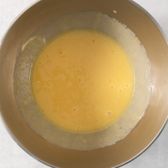 A metal mixing bowl containing a smooth, yellow batter is placed on a light-colored surface.