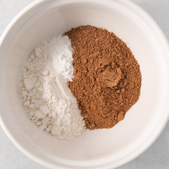 A white bowl contains separate portions of white flour and cocoa powder.