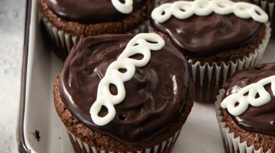 Chocolate cupcakes with a swirl of white icing are arranged in a white baking tray.