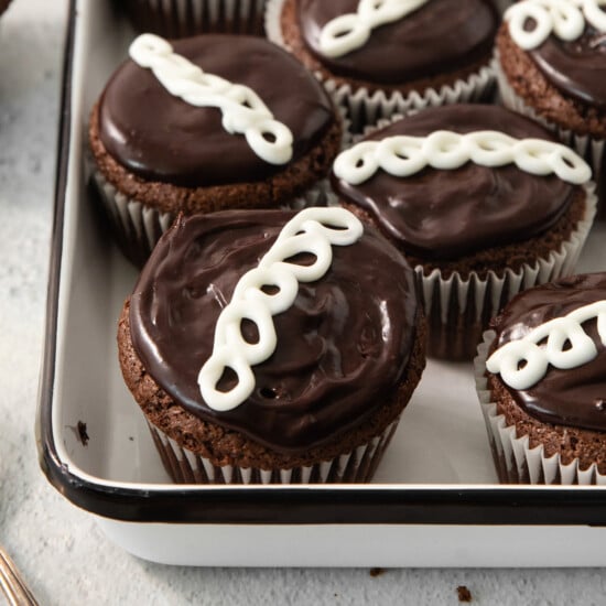 Chocolate cupcakes with a swirl of white icing are arranged in a white baking tray.